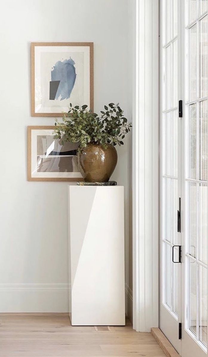 a vase with some plants on top of it next to a door and framed pictures