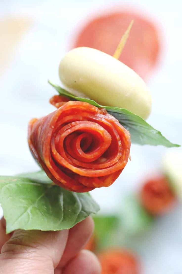 a person holding up a piece of food that looks like a rose with leaves on it