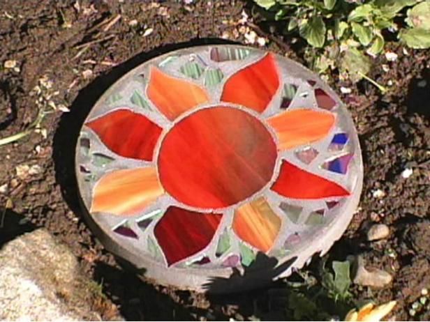 a glass sunflower sitting on top of a rock in the dirt next to plants