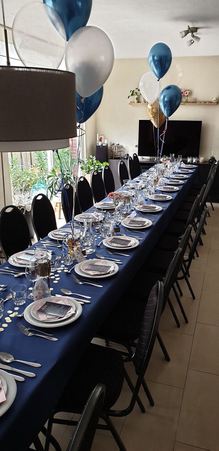 a long table set with plates, silverware and blue balloons for a formal function