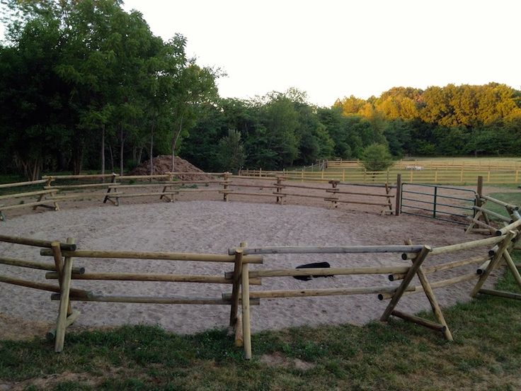 a wooden fenced in area with an empty horse paddock on the grass and trees behind it