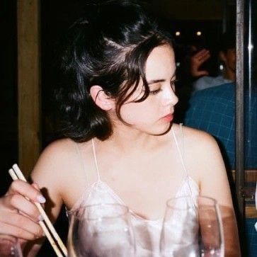 a woman sitting at a table with chopsticks in her hand while looking down