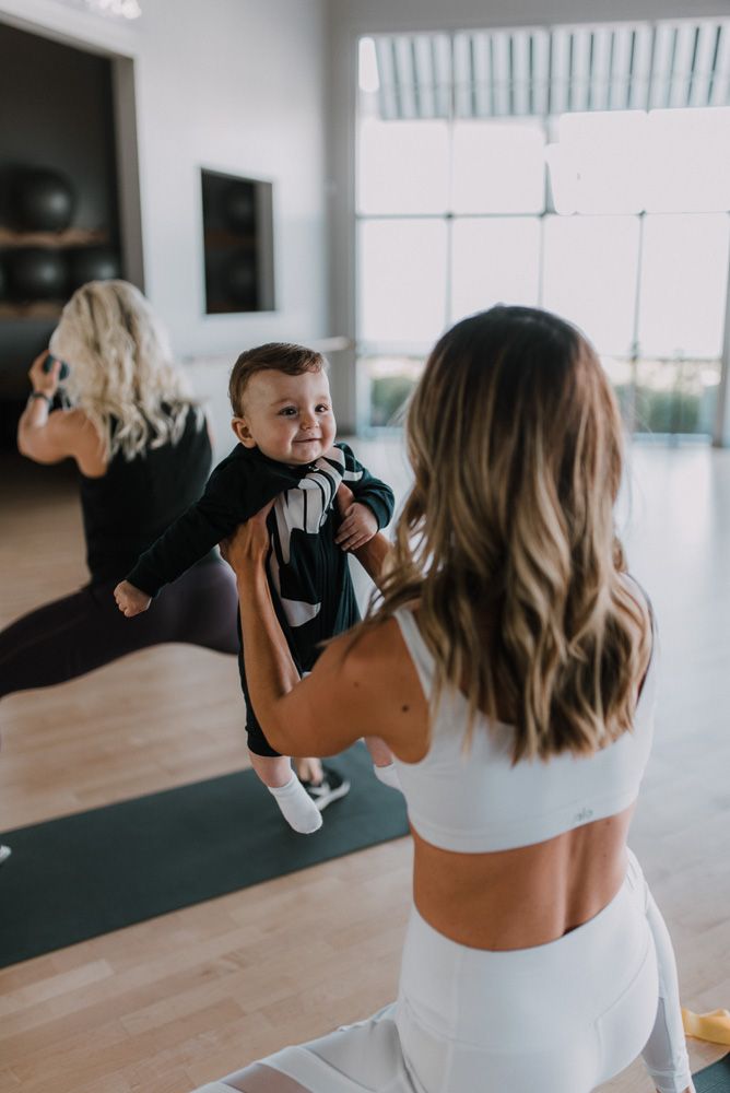 a woman holding a child in the middle of a yoga class