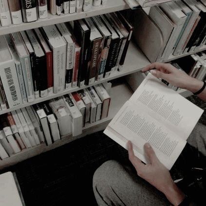 a person sitting on the floor reading a book in front of a bookshelf