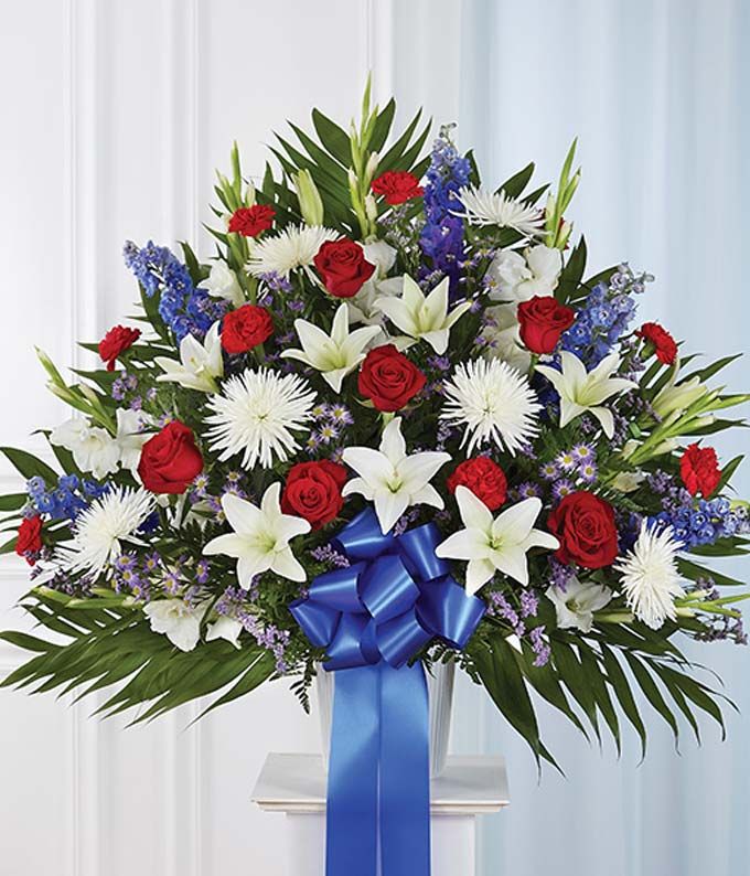 a bouquet of red, white and blue flowers in a vase with a blue ribbon