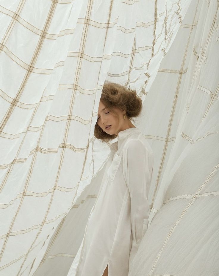 a woman standing in front of a curtain with her hair pulled back and eyes closed