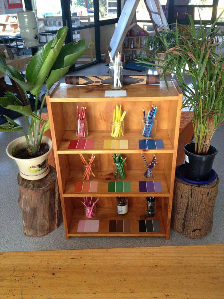 a wooden shelf filled with lots of different types of pens and pencils next to potted plants