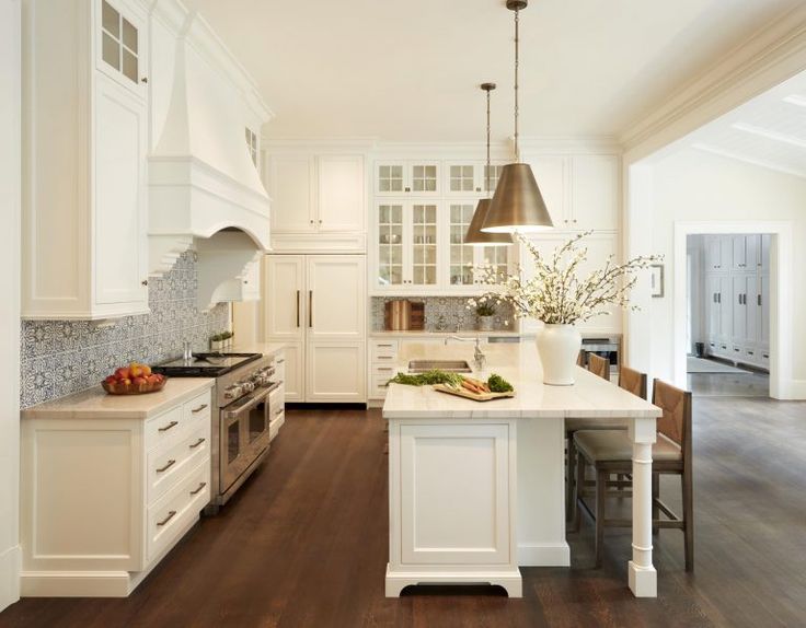 a large kitchen with white cabinets and wood flooring is pictured in this image, there are two lights hanging over the island