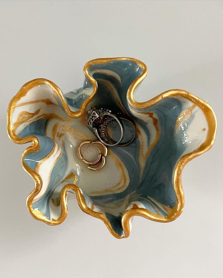 two wedding rings are placed in the center of a ceramic flower shaped bowl with gold and blue accents