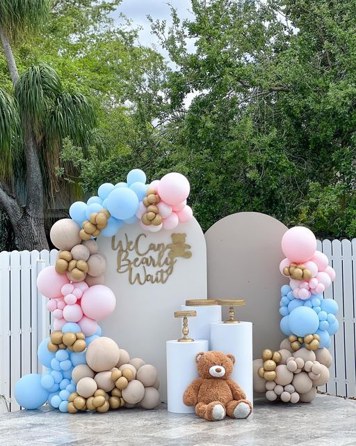 a teddy bear sitting in front of a welcome sign with balloons on it and a cake