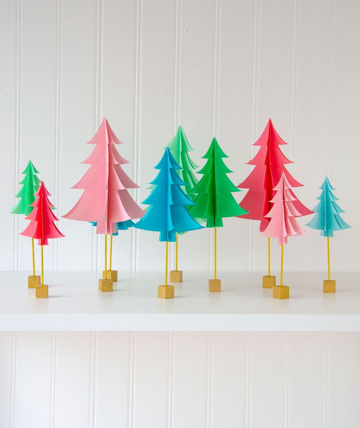 colorful paper trees lined up on top of each other in front of a white wall