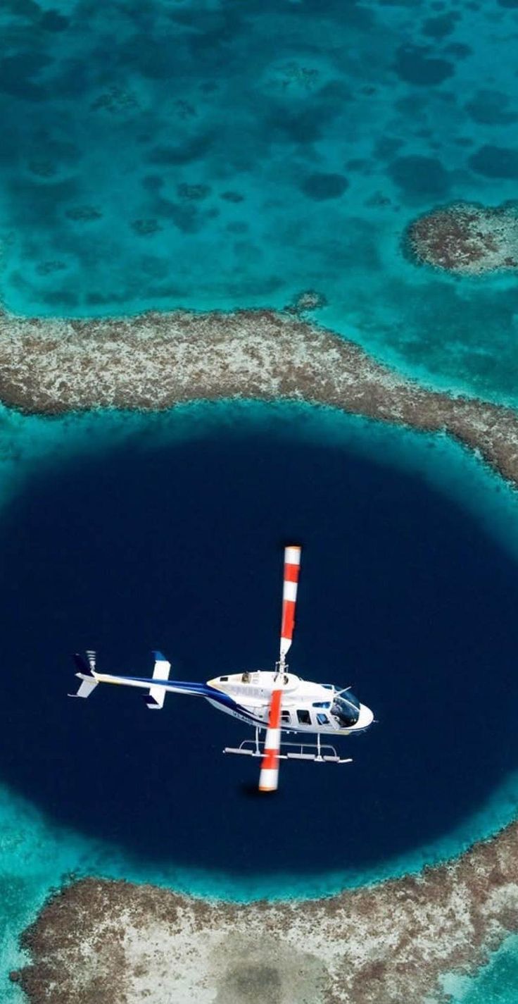 an aerial view of a helicopter flying over a blue hole in the ocean with corals