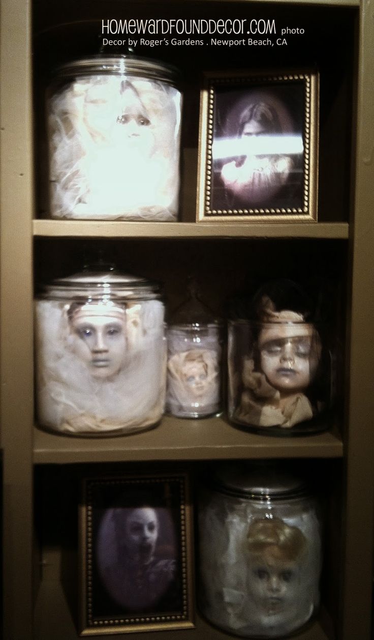 some jars with faces on them are in a cabinet together and one is painted white