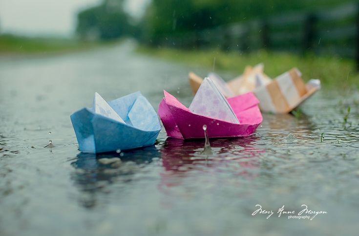 three origami boats sitting on the side of a rain soaked road in the rain