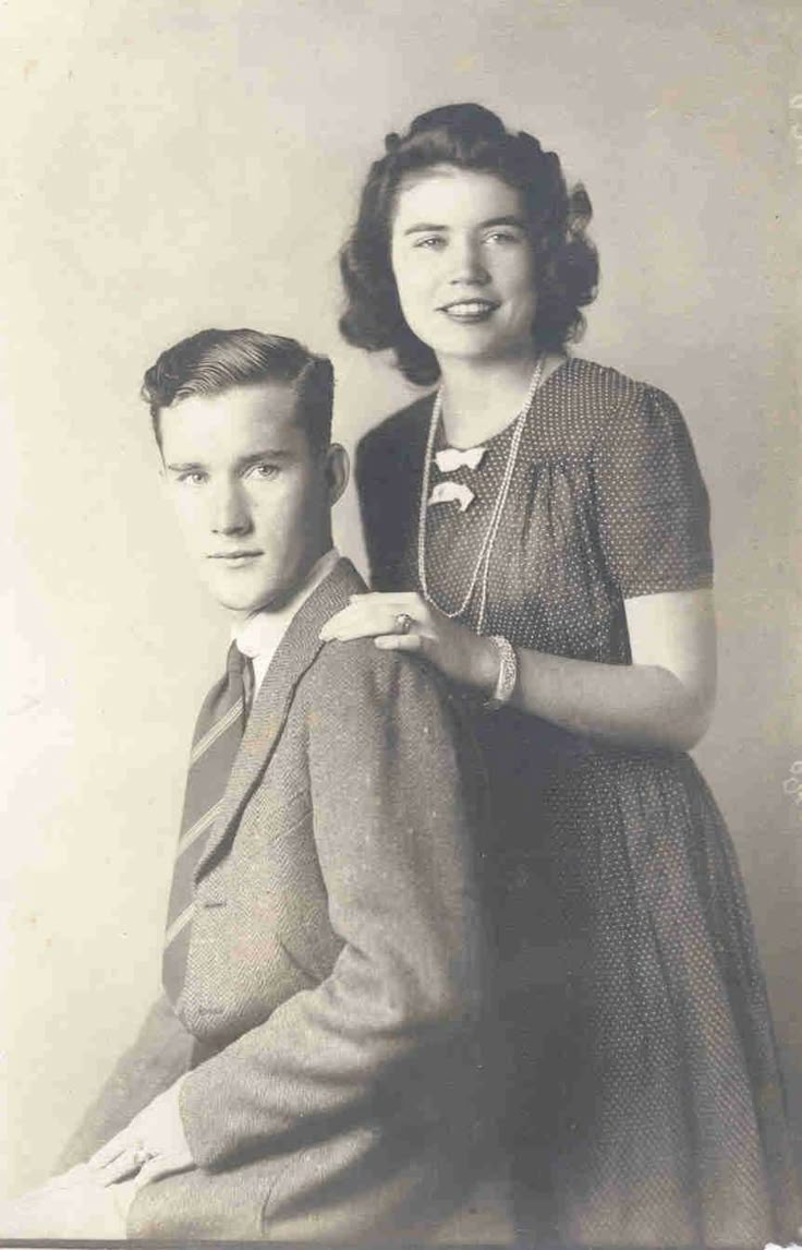 an old black and white photo of a man standing next to a woman in a dress