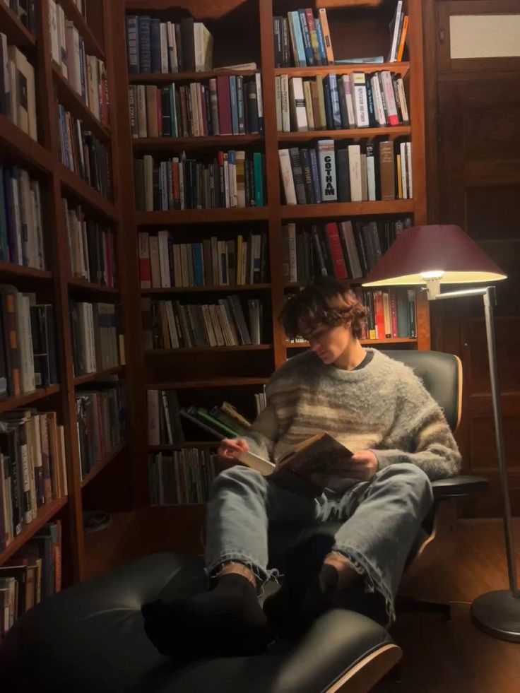 a person sitting in a chair reading a book near a lamp and bookshelf