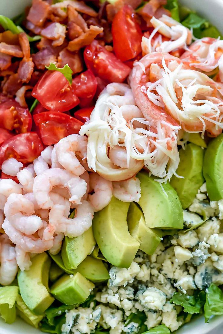 a salad with shrimp, avocado, tomatoes and other toppings in a white bowl