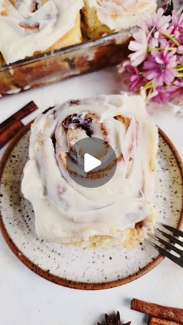 a plate topped with cinnamon rolls covered in frosting and cinnamon sticks next to flowers