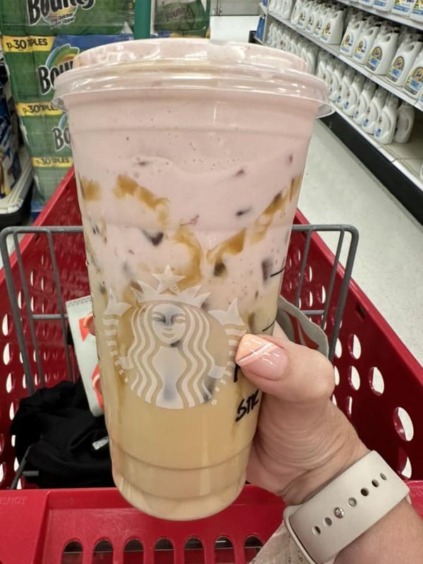 a person holding up a starbucks drink in a grocery cart at a store with other items on the shelves