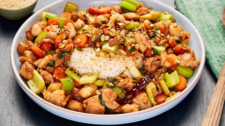 a bowl filled with rice and vegetables next to a wooden spoon on top of a table