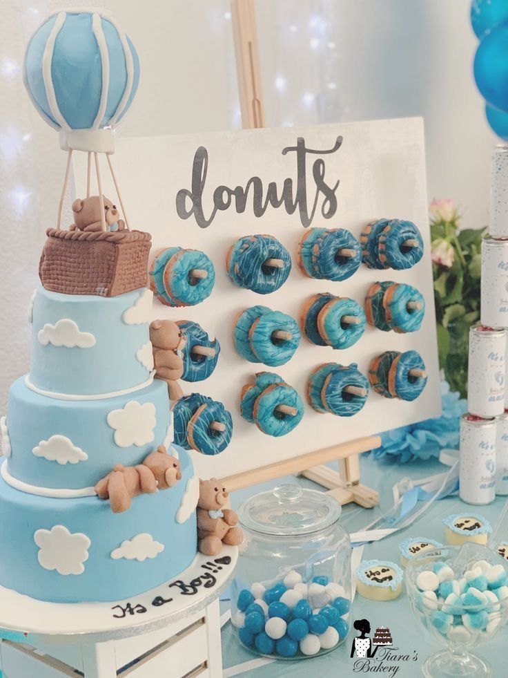 a blue and white dessert table with donuts on the top, hot air balloons in the background