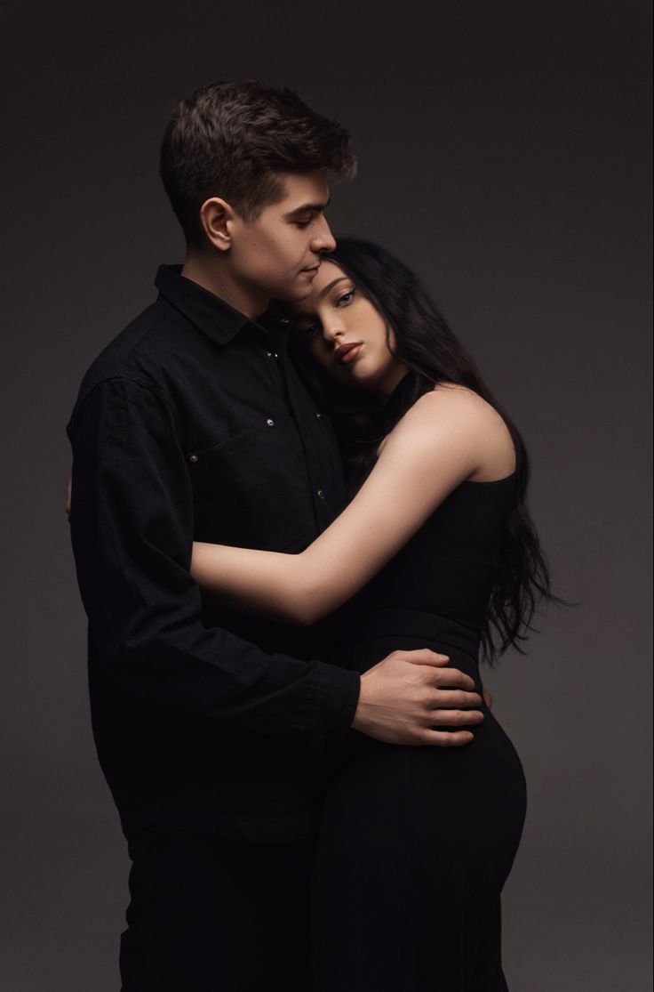 a man and woman embracing each other in front of a dark background with their arms around one another