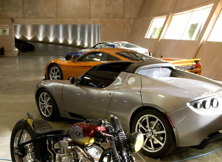 two motorcycles parked next to each other in a parking garage with sports cars behind them