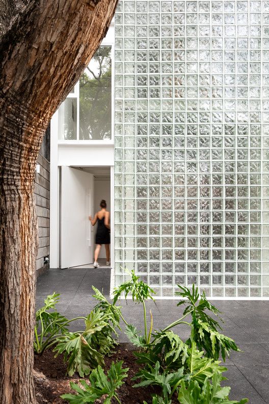 a woman standing in an open doorway next to a tree and building with glass blocks on it