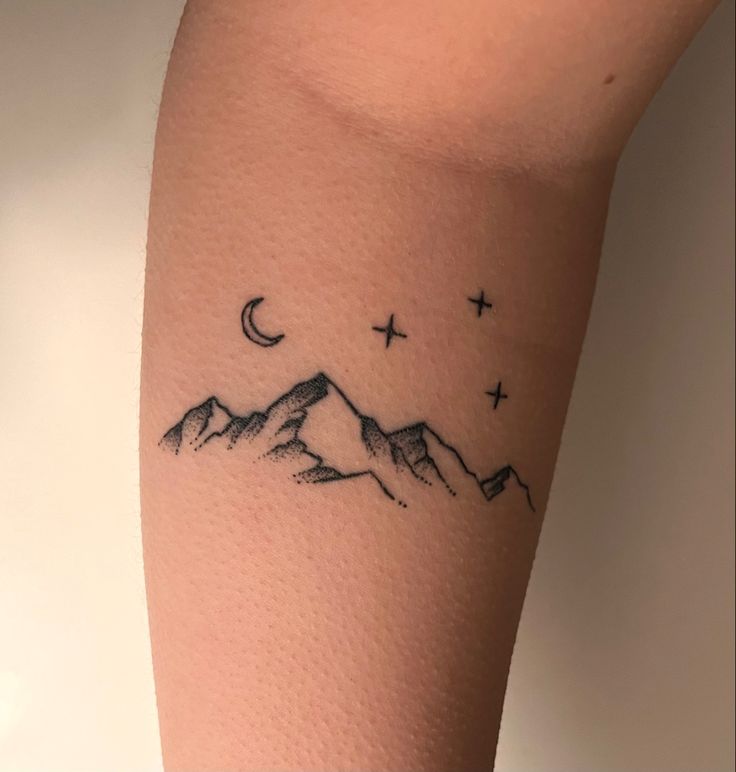 a tattoo on the leg of a person with mountains and stars in the sky above them