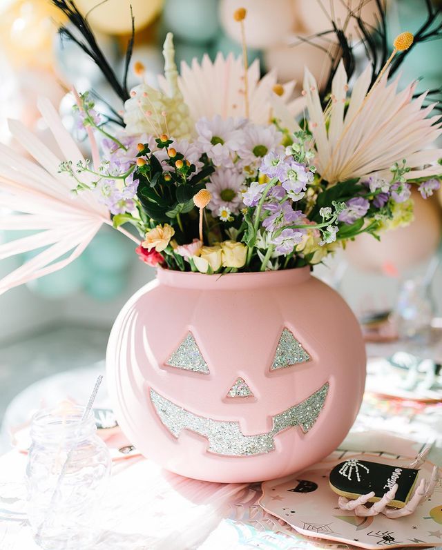 a pink pumpkin vase filled with flowers on top of a table next to other decorations