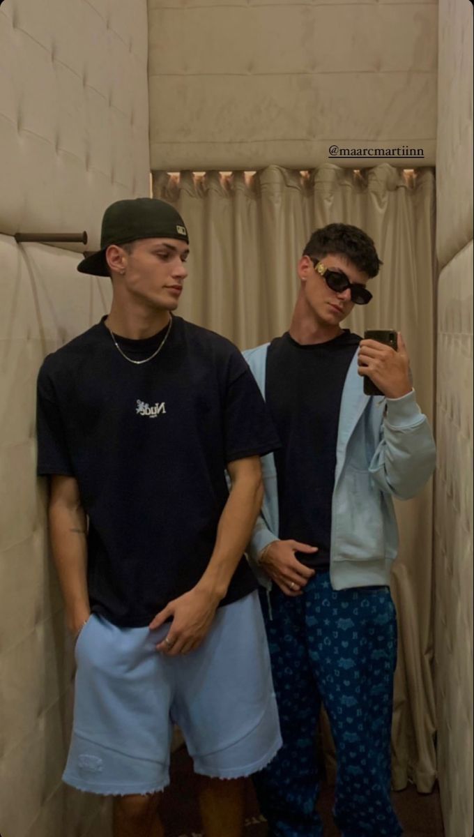 two young men standing next to each other in front of a shower curtain and looking at their cell phones