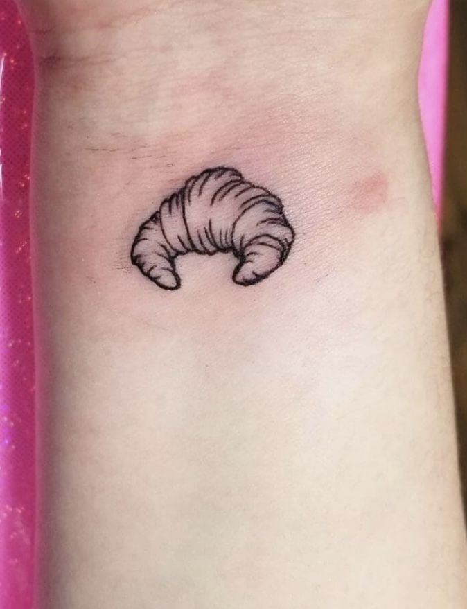 a small black and white cat tattoo on the left wrist, it looks like a croissant