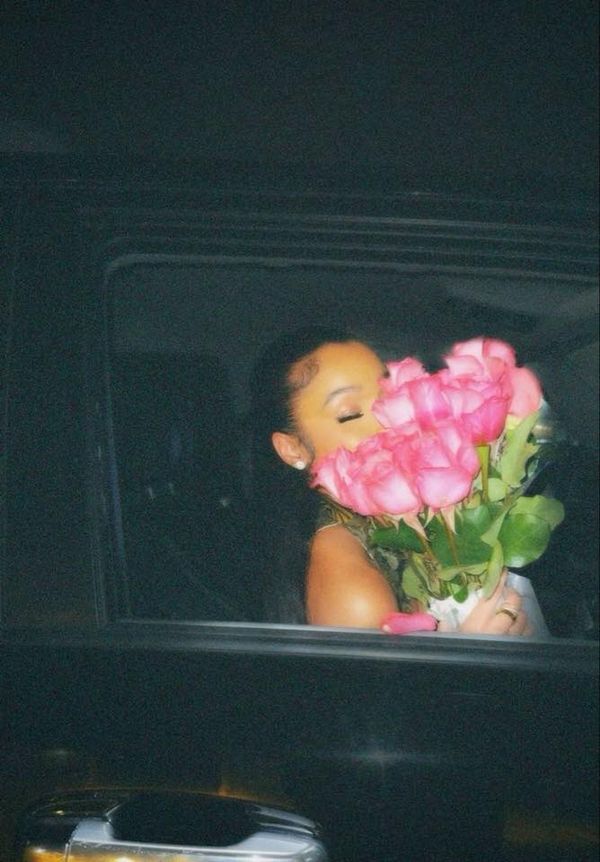 a woman is holding pink roses in the back of a truck with her eyes closed