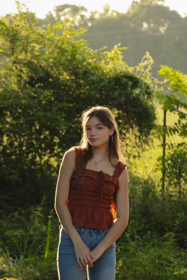 a woman standing in the grass with her hand on her hip and looking off into the distance