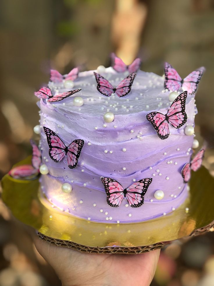 a hand holding a purple cake with pink butterflies on it and pearls around the edges