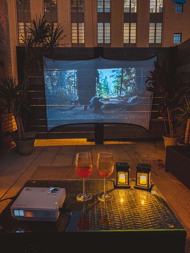 two wine glasses sitting on top of a table next to a projector screen