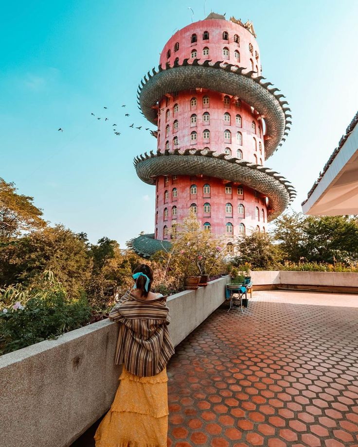 a woman standing in front of a tall pink tower with birds flying around the top