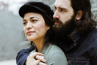 a man with long hair and beard standing next to a woman wearing a black hat