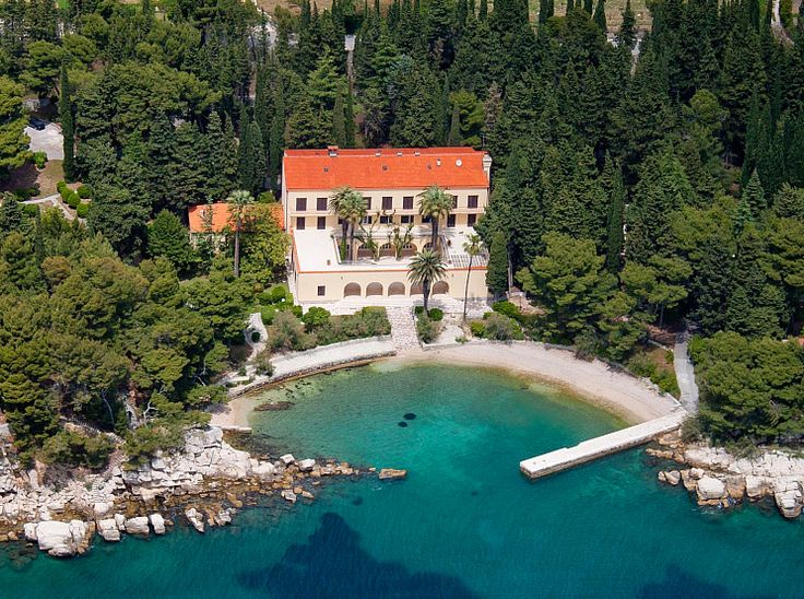 an aerial view of a house in the middle of some trees and water with a plane flying over it