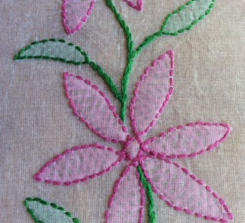 a pink flower with green leaves is embroidered onto a piece of cloth that has been stitched together