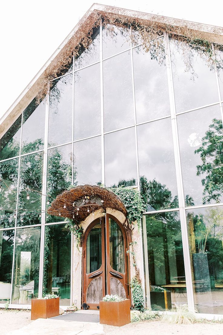 a large glass building with a wooden door and window panes on the outside, surrounded by greenery