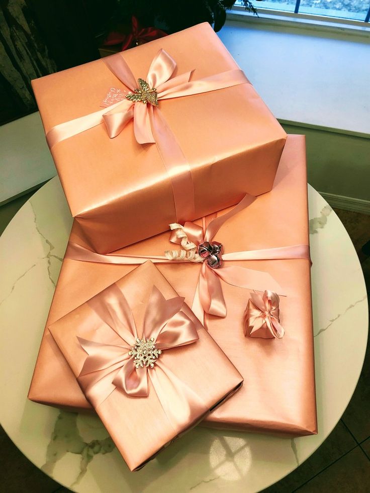 three pink wrapped presents sitting on top of a white table next to a large window