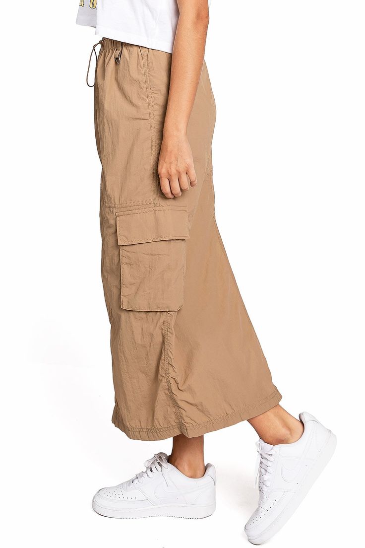 Chic, parachute skirt with an elastic waistband, a drawstring cinch tie and cargo pockets down the sides. Pair it with a graphic tee and sneakers for an effortless streetwear look. CARE | Machine Wash Cold CONTENTS | 100% Nylon MEASUREMENTS | 33"/85 cm Top to Bottom (Size Small) MODEL | 5'8 - wearing a size Small IMPORTED Casual Baggy Bottoms With Functional Drawstring, Casual Summer Cargo Parachute Pants, Casual Cargo Skirt With Drawstring For Summer, Casual Drawstring Cargo Skirt For Summer, Casual Summer Cargo Skirt With Drawstring, Casual Nylon Cargo Pants For Summer, Casual Summer Cargo Pants With Functional Drawstring, Summer Casual Nylon Cargo Pants, Spring Utility Cargo Skirt With Drawstring