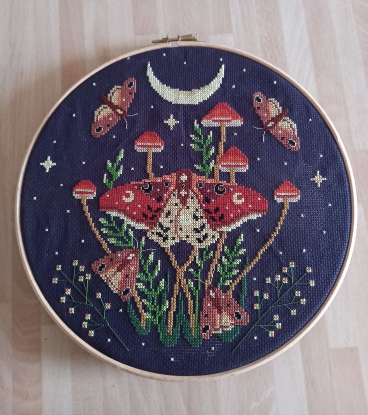 a close up of a embroidery on a wooden surface with mushrooms and butterflies in the background