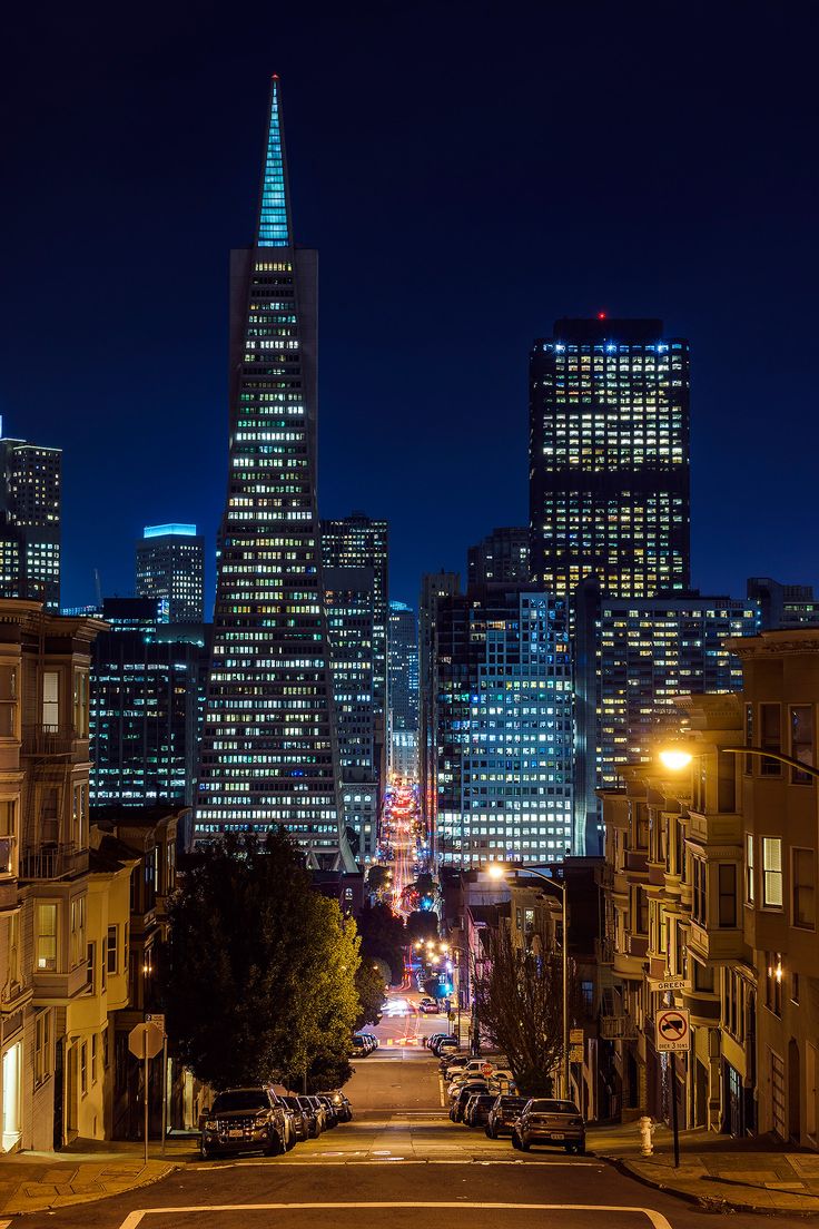 the city skyline is lit up at night, with cars parked on the street below