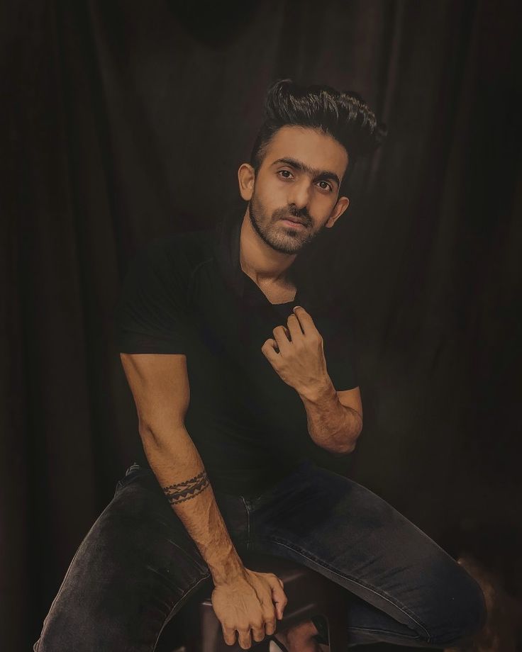 a man sitting on top of a stool in front of a black background with his hand on his chin