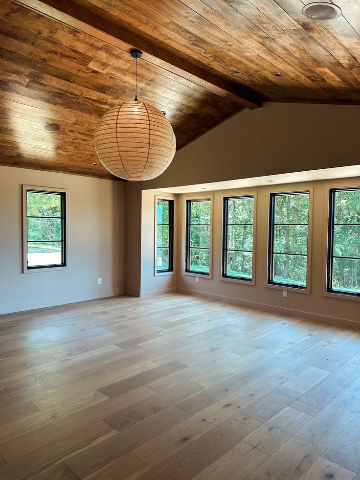 an empty room with wood floors and three windows in the center is lit by two pendant lights