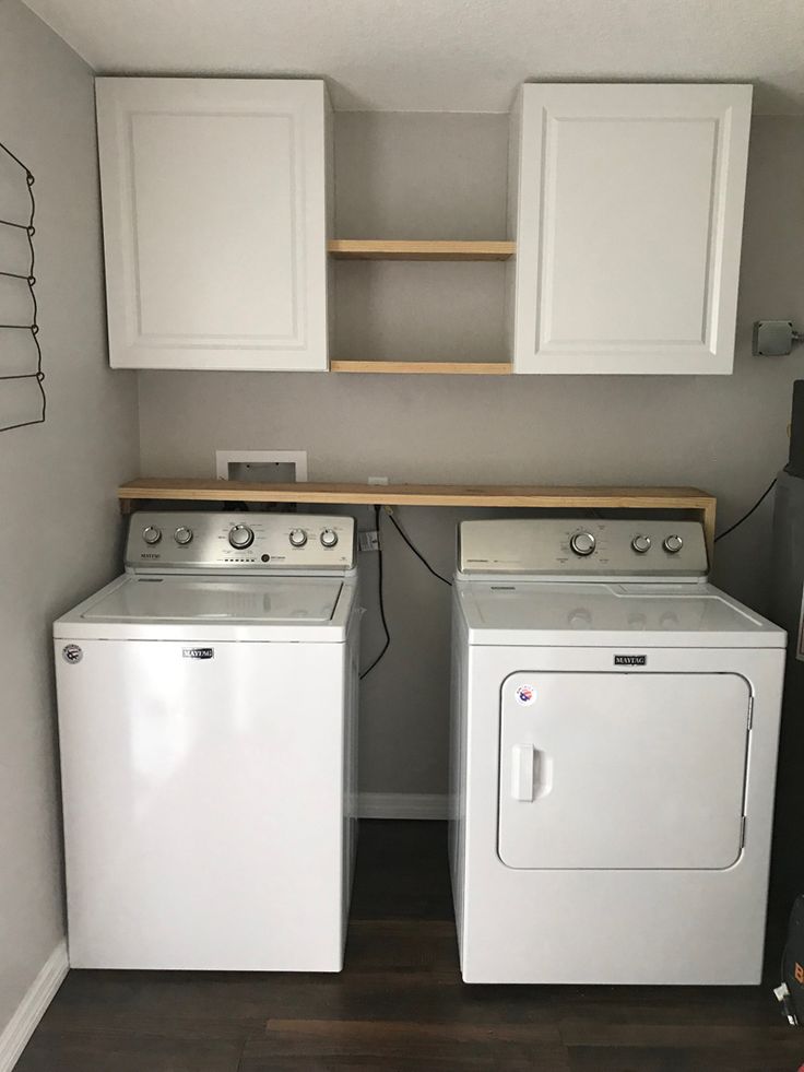 two washers and a dryer in a small room with white cabinets on the wall