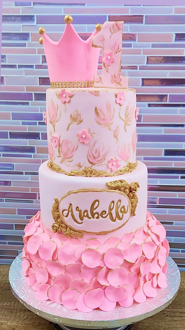 a three tiered cake with pink flowers and a crown on top