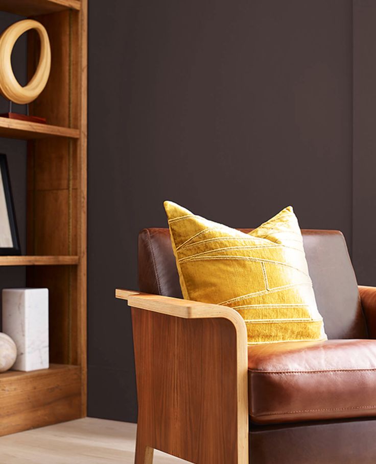 a brown leather chair sitting in front of a wooden book shelf with books on it